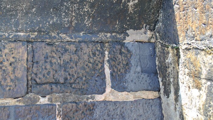 A historical bluestone wall showing indistinct, weathered engraving on one of the cobblestones.
