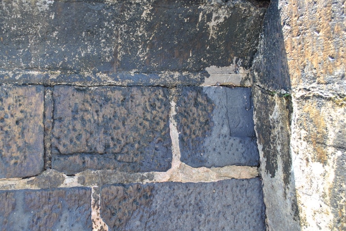 A historical bluestone wall showing indistinct, weathered engraving on one of the cobblestones.