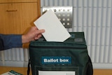 Close up of hand dropping completed vote paper into ballot box for ACT election. Oct 2012.