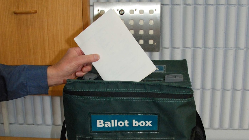 Close up of hand dropping completed vote paper into ballot box for ACT election. Oct 2012.