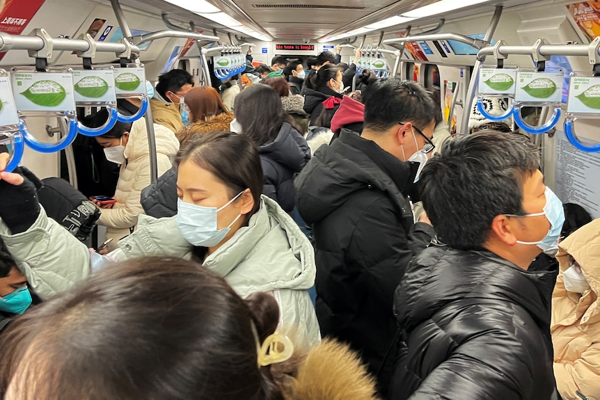 People are tightly packed on a subway train in china, all wearing face masks.