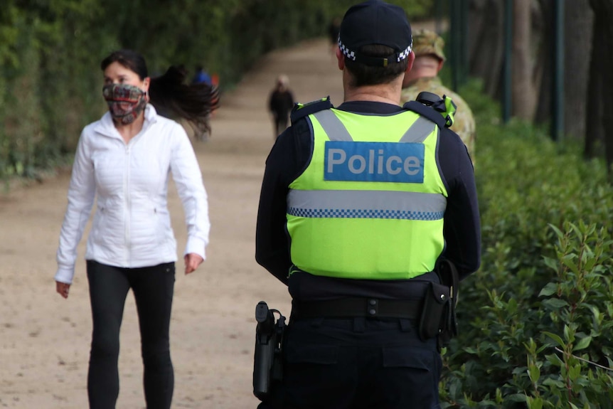 A police officer's back wearing a fluro vest which says police, stands on the tan near walkers.