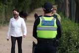 A police officer's back wearing a fluro vest which says police, stands on the tan near walkers.