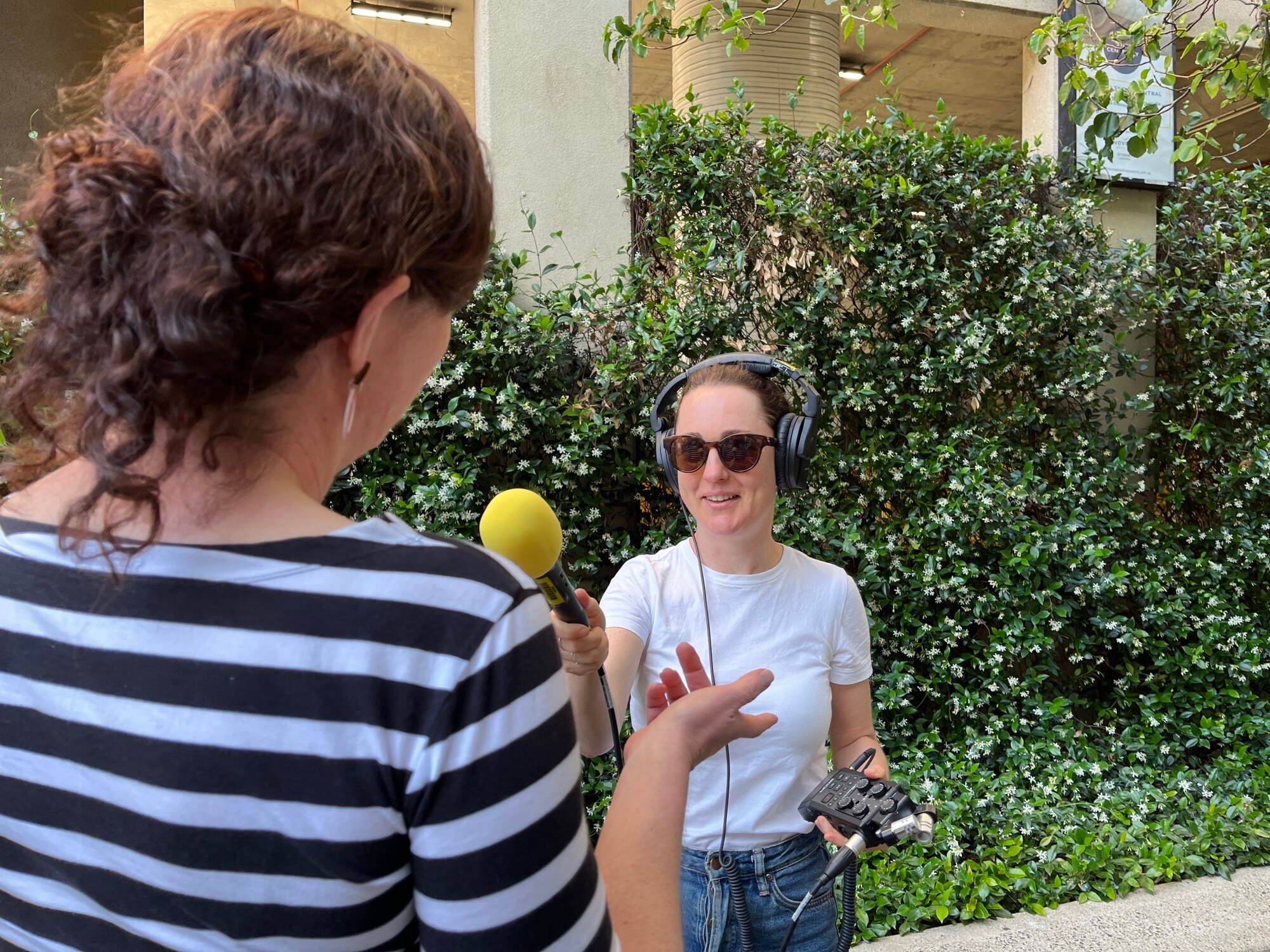Woman with headphones on, holding a microphone and interviewing another woman.