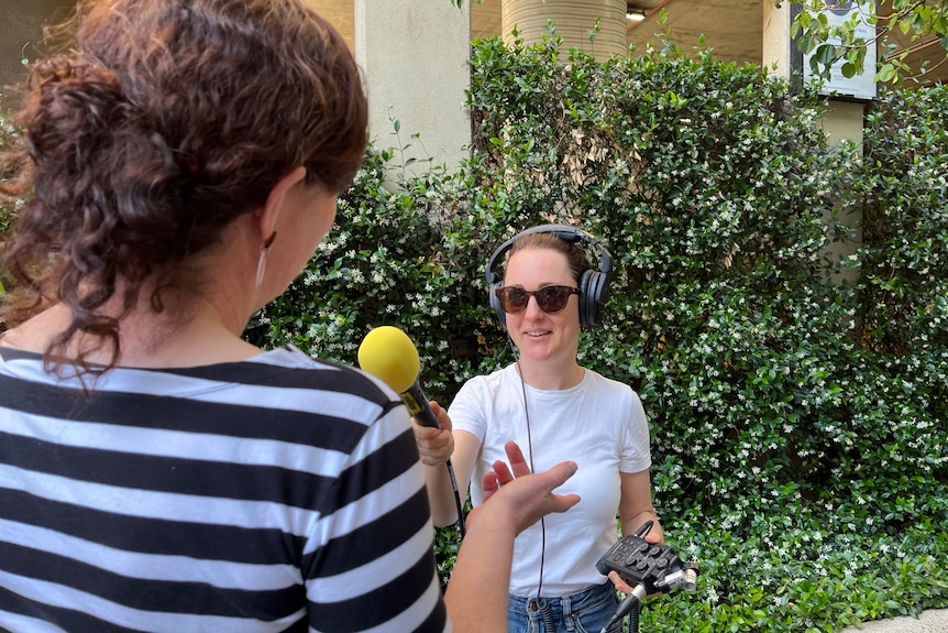 Woman with headphones on, holding a microphone and interviewing another woman.