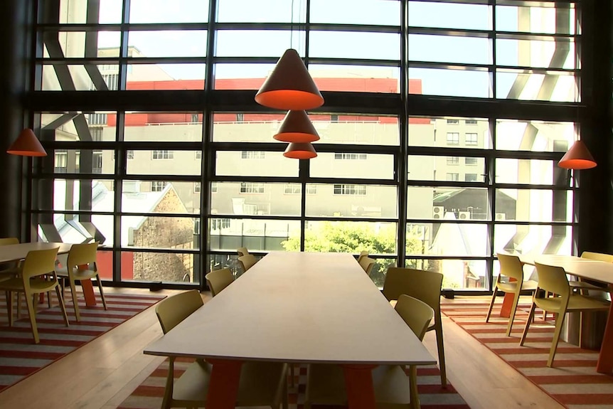 Empty tables and chairs in front of a floor to ceiling window.