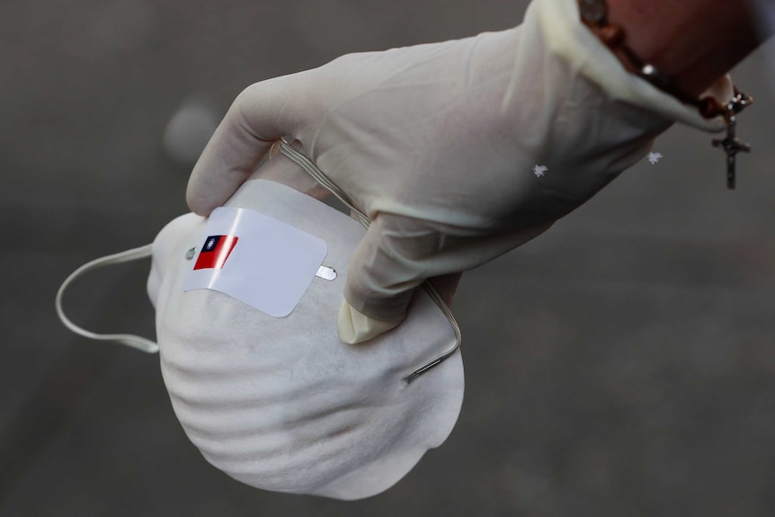 A generic image of a hand with a rubber glove holding a face mask.