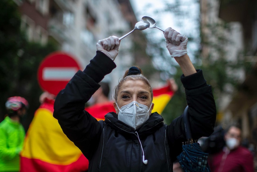A woman in a mask protests by banging spoons together in Spain