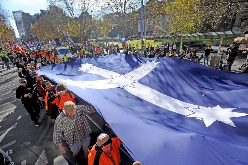 Building and construction workers march down Swanston Street with a Southern Cross flag unfurled.