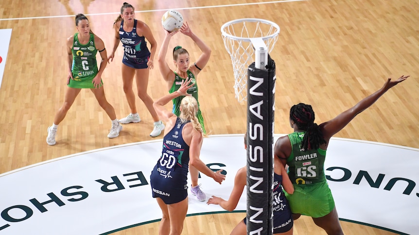 Netballer shooting a shot while being defended and her teammate holding under the post 