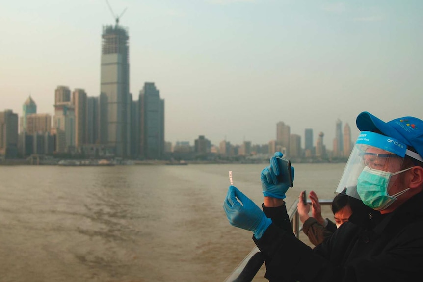 A masked tourist takes a photo of his ticket aboard a ferry on the Yangtze River in front of Wuhan's skyline.