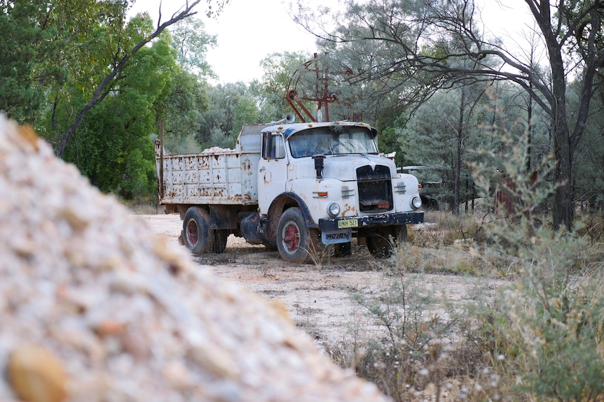 White pile of rocks in foreground, old white truck in background with trees.