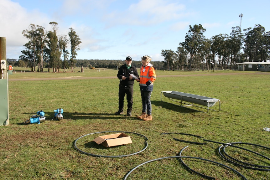 Two people stand near a water trough.