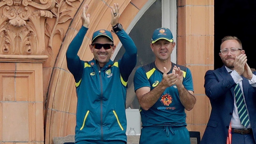 Australian cricket coach and his assistant coach applaud on the balcony at Lord's after a wicket.