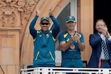 Australian cricket coach and his assistant coach applaud on the balcony at Lord's after a wicket.