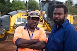 Darren Macumboy and Wilfred Accoom stand in front of the heavy machinery they are using to redevelop roads near Lockhart River.