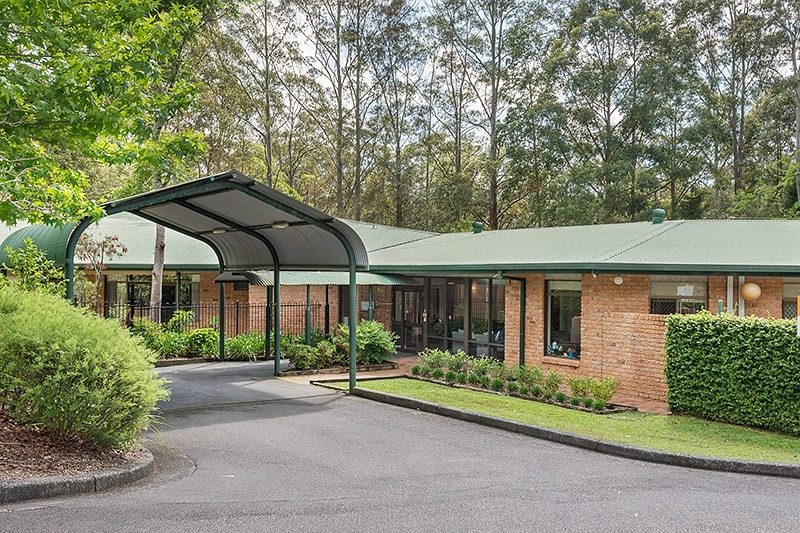 A brick building with a green roof, hedge, lawn and driveway.