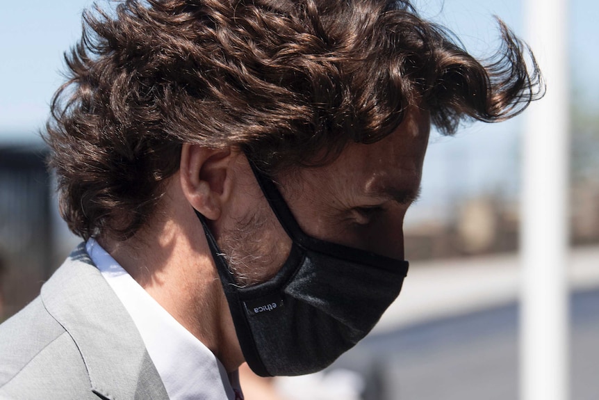 A close up side profile of a man, looking down and wearing a black mask that covers his nose and mouth