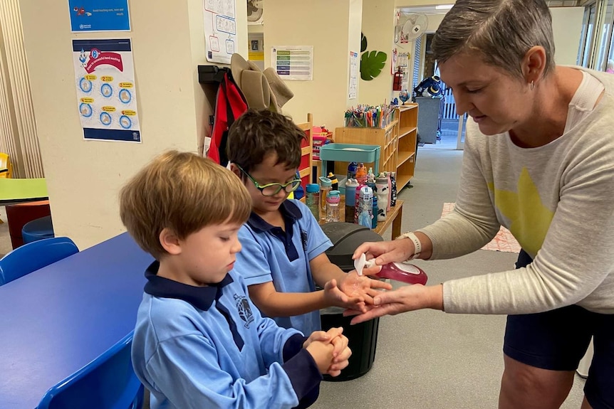 A woman squirting hand sanitiser onto the hands of two small boys