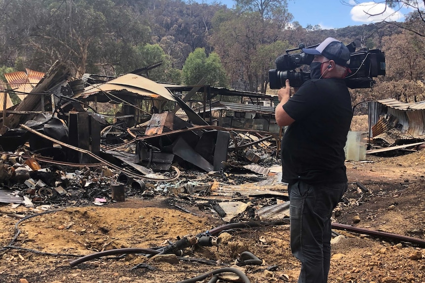Cameraman filming in ruins of a burnt out house.