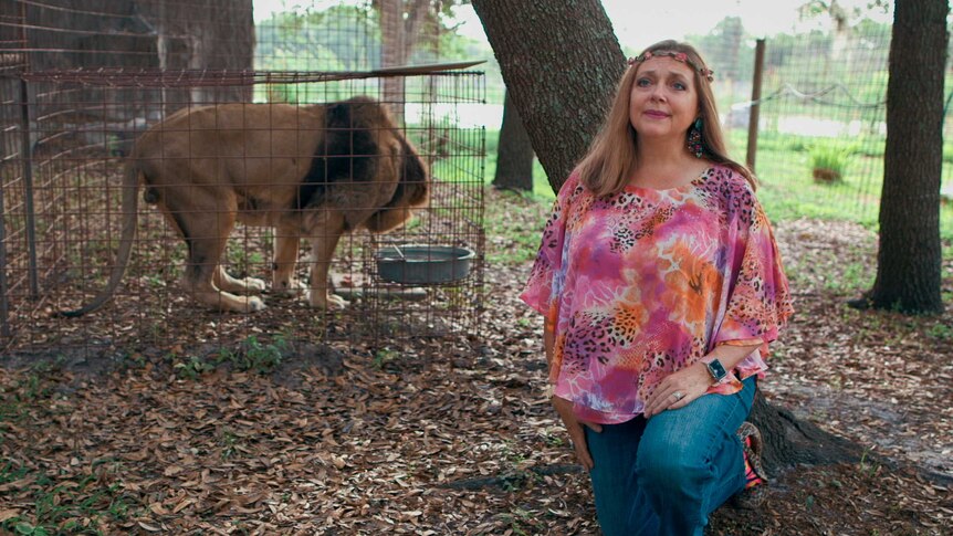 Carole Baskin kneels in front of a lion