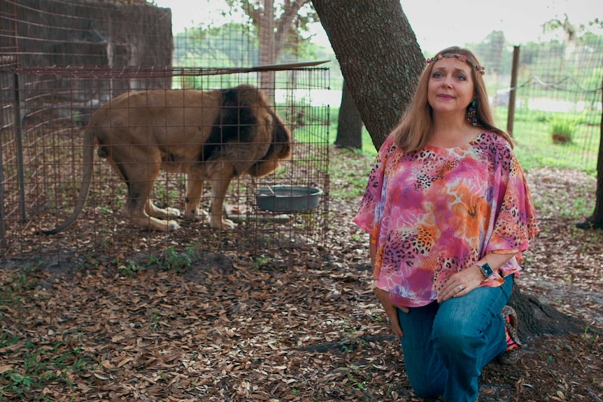 Carole Baskin kneels in front of a lion