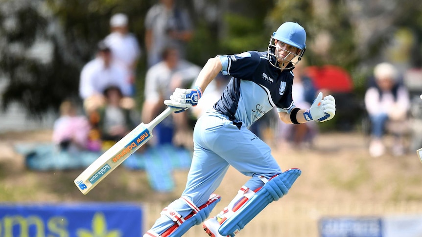 A cricket player wearing blue kit runs between the wickets with his bat trailing behind him