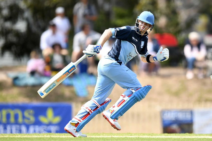 A cricket player wearing blue kit runs between the wickets with his bat trailing behind him