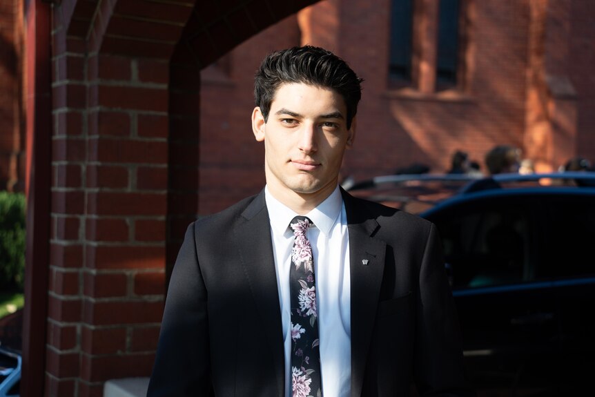 a young man in a suit looks at the camera beside a church