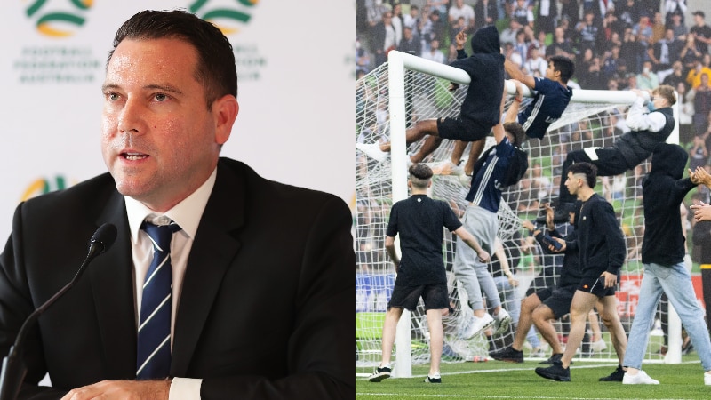 A man in a suit talks during a press conference next to an image of soccer fans swinging from a goal