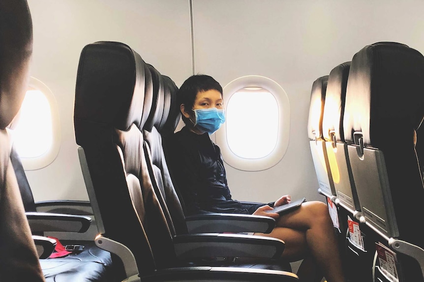 Female passenger wearing mask sitting in airplane and looking directly at the camera.