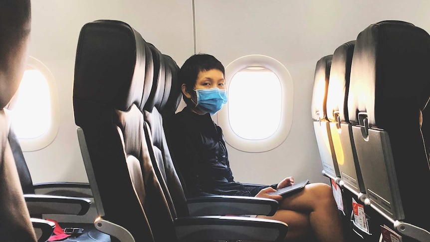 Female passenger wearing mask sitting in airplane and looking directly at the camera.