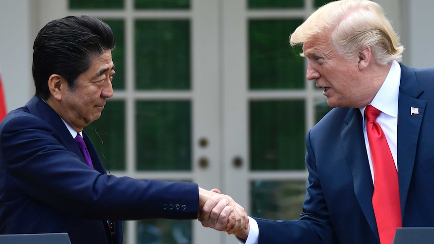 Japanese Prime Minister Shinzo Abe reaches to the right of a podium to shake hands with US President Donald Trump.