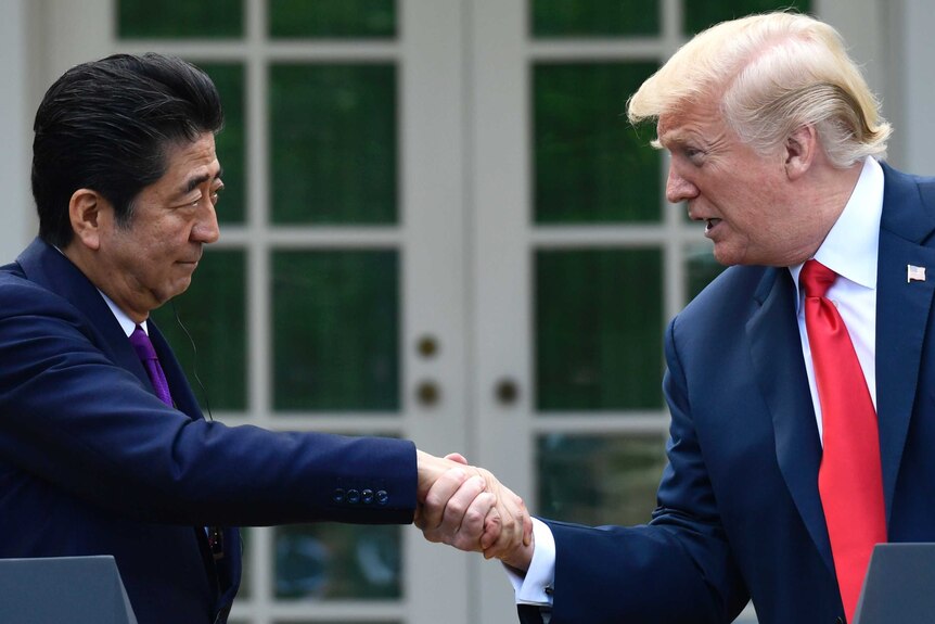 Japanese Prime Minister Shinzo Abe reaches to the right of a podium to shake hands with US President Donald Trump.
