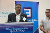 A man in suit and a man in grey shirt at a press conference in Suva. 