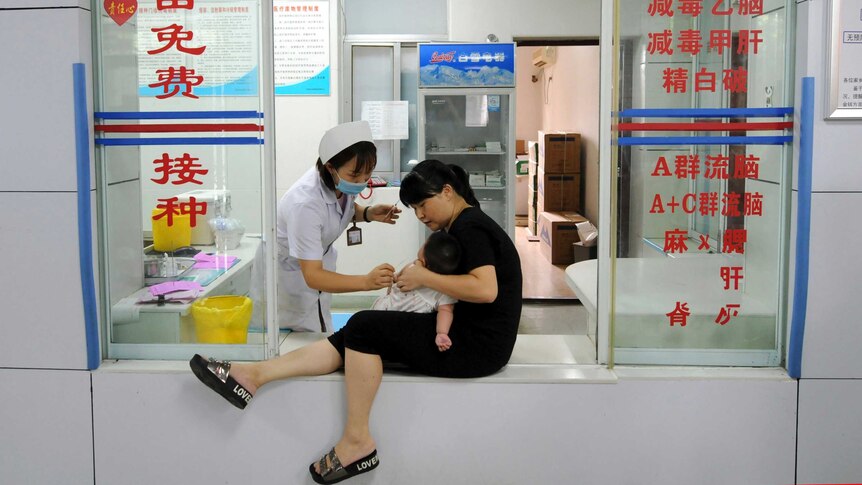 A woman holds an infant as a nurse administers a vaccination at a Chinese Center for Disease Control