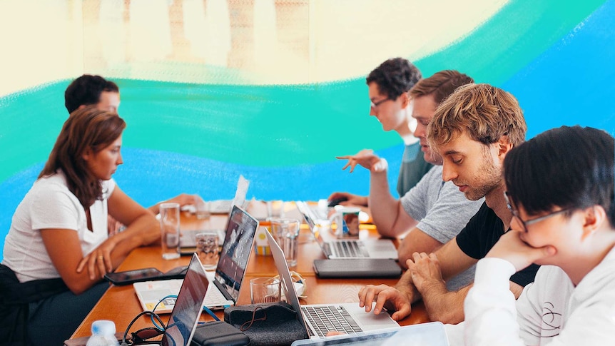 Group of men and women working on their laptops at a large desk for a story about the dark side of entrepreneurship