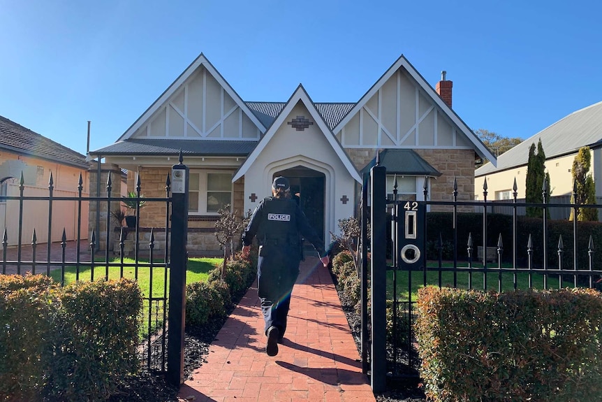 A police officer walking through the front gate of a house