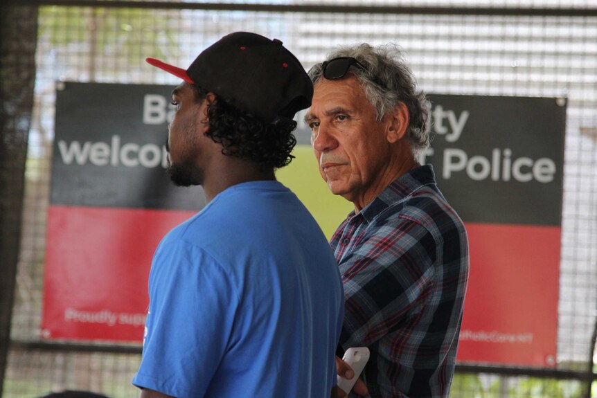 A young man and an old man stand together and talk.