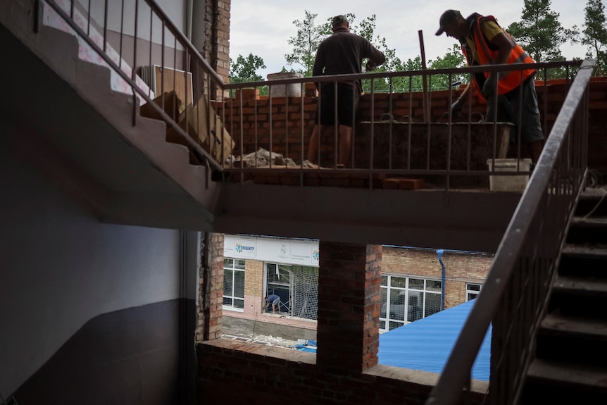 Workers replace windows , lay bricks in a blown-out school building