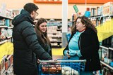 Three friends talking in an aisle while standing around a supermarket trolley for story on tension during coronavirus pandemic