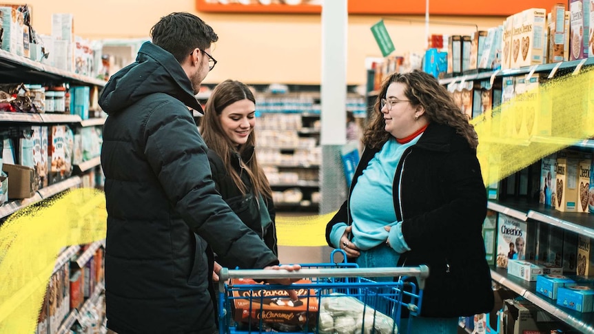 Three friends talking in an aisle while standing around a supermarket trolley for story on tension during coronavirus pandemic