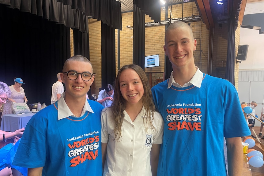 Three teenagers stand together and smiling at the camera. Isabelle Doherty, a cancer survivor, stands in between her classmates.