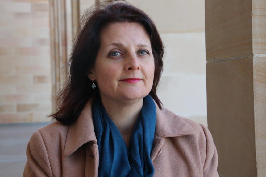 Ms McGurk looks at the camera, smiling slightly, in front of the sandstone steps of Parliament. She wears a scarf and jacket.