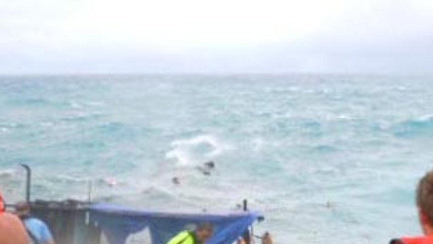 Onlookers watch as a boat carrying scores of asylum seekers breaks apart after smashing into rocks off Christmas Island.