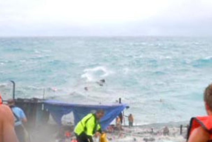 Onlookers watch as a boat carrying scores of asylum seekers breaks apart after smashing into rocks off Christmas Island.