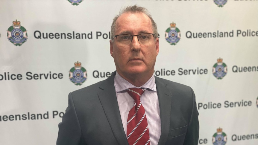 A police officer in a suit looks at the camera with a serious expression.