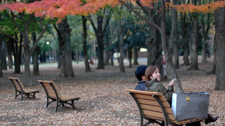 A young couple enjoying a smoke in the autumn colour after shopping.