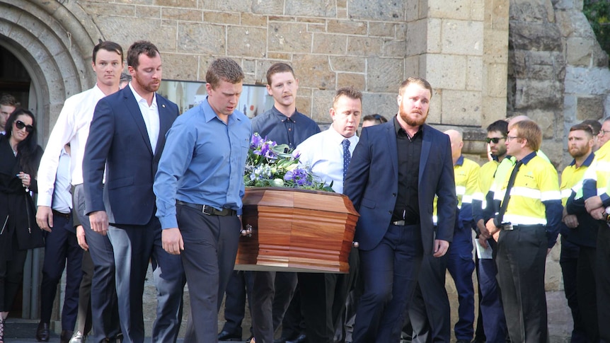 A group of men carry a coffin out of a church.