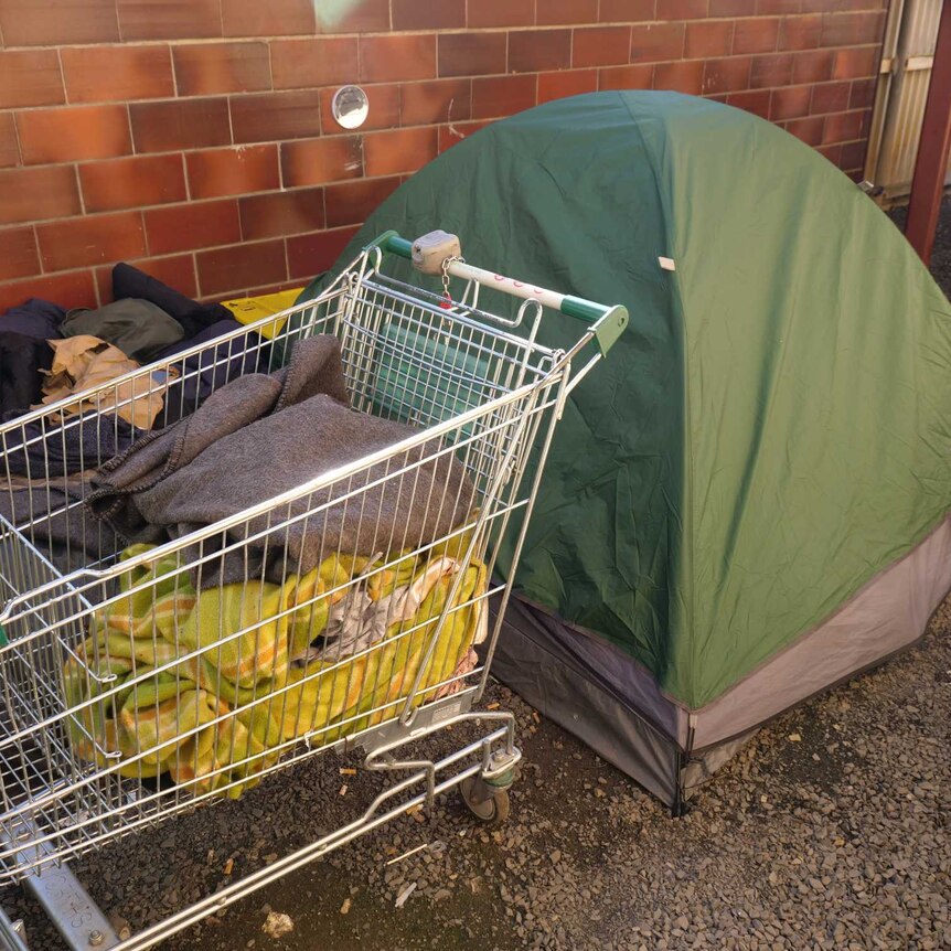 A tent next to a shopping trolley with a suitcase and clothes